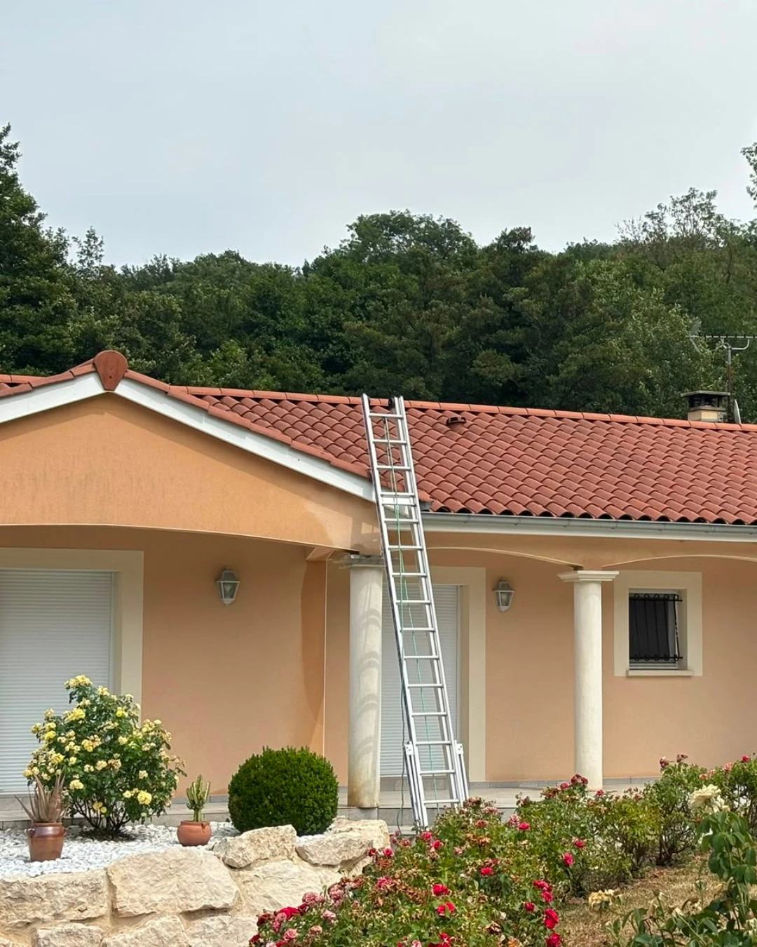 Maison couverte en tuiles canal avec une échelle de couvreur posée contre la gouttière