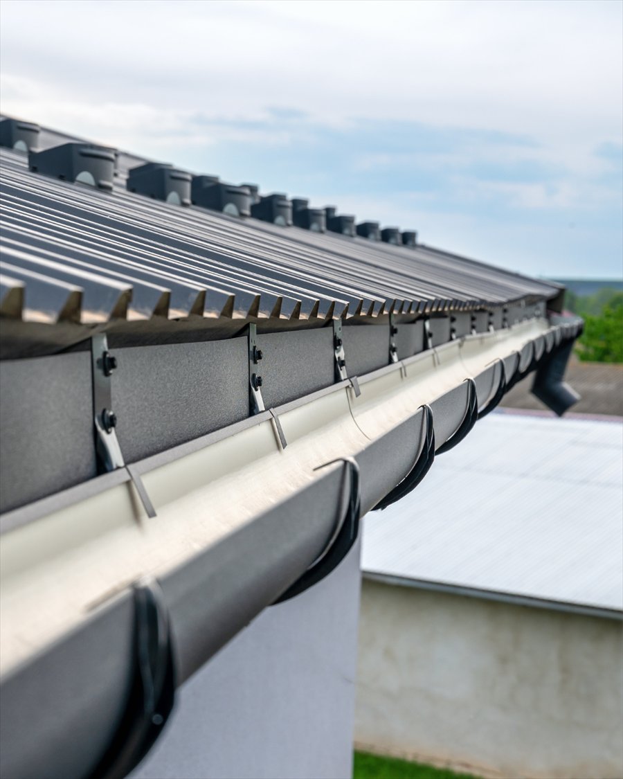 Gouttière neuve et crochets de fixation le long d’une toiture en bac acier