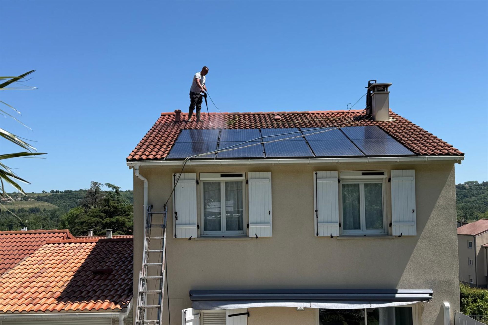 Couvreur nettoyant au jet haute pression la toiture en tuiles d'une maison
